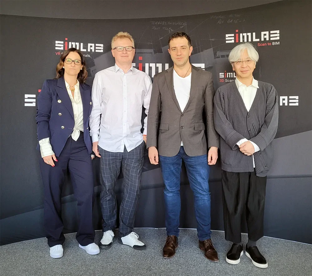 Four people posing in front of a SIMLAB backdrop at the SIMLAB head office: Karolina Drwięga-Waliczek, Marek Koźlak, Łukasz Gawlik and Jun Inoue