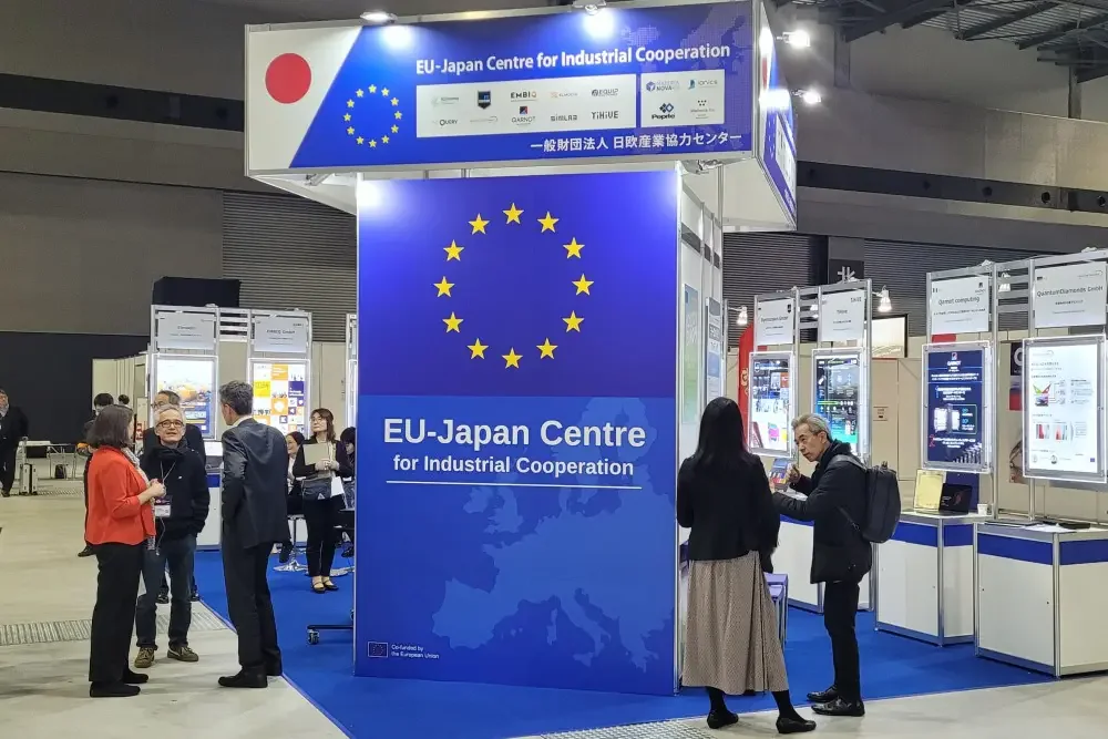 EU-Japan Centre for Industrial Cooperation booth with EU stars and the Japanese flag, visitors talking at the exhibitor kiosks