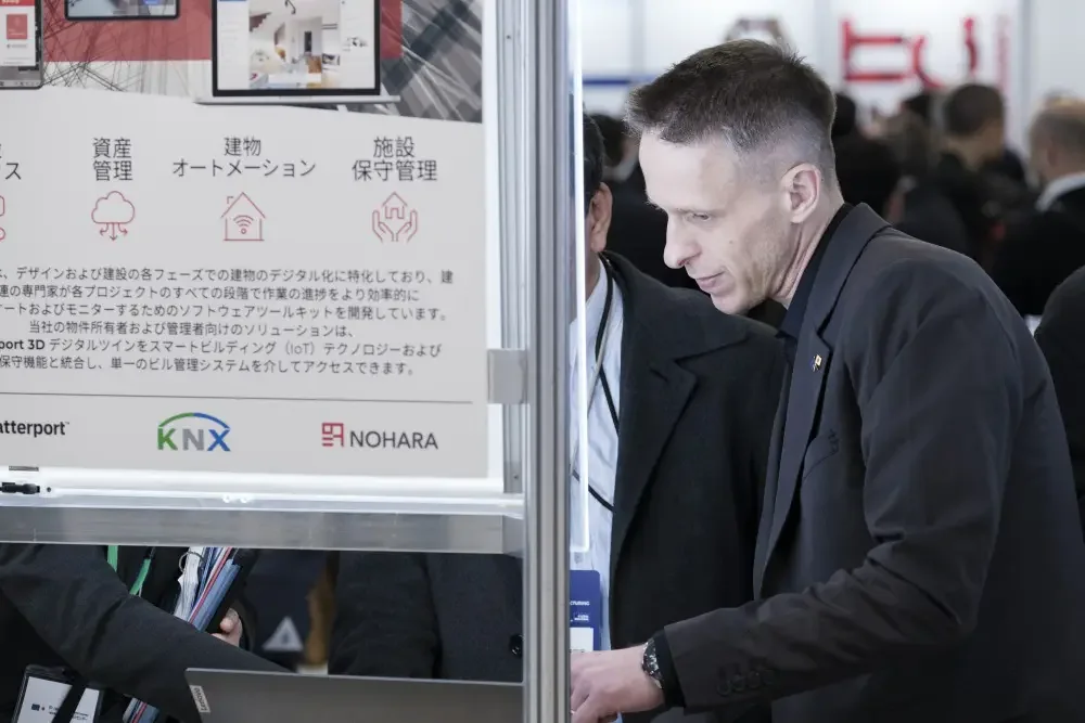 Man in a dark blazer working on a laptop next to the SIMLAB poster with Matterport, KNX and NOHARA logos