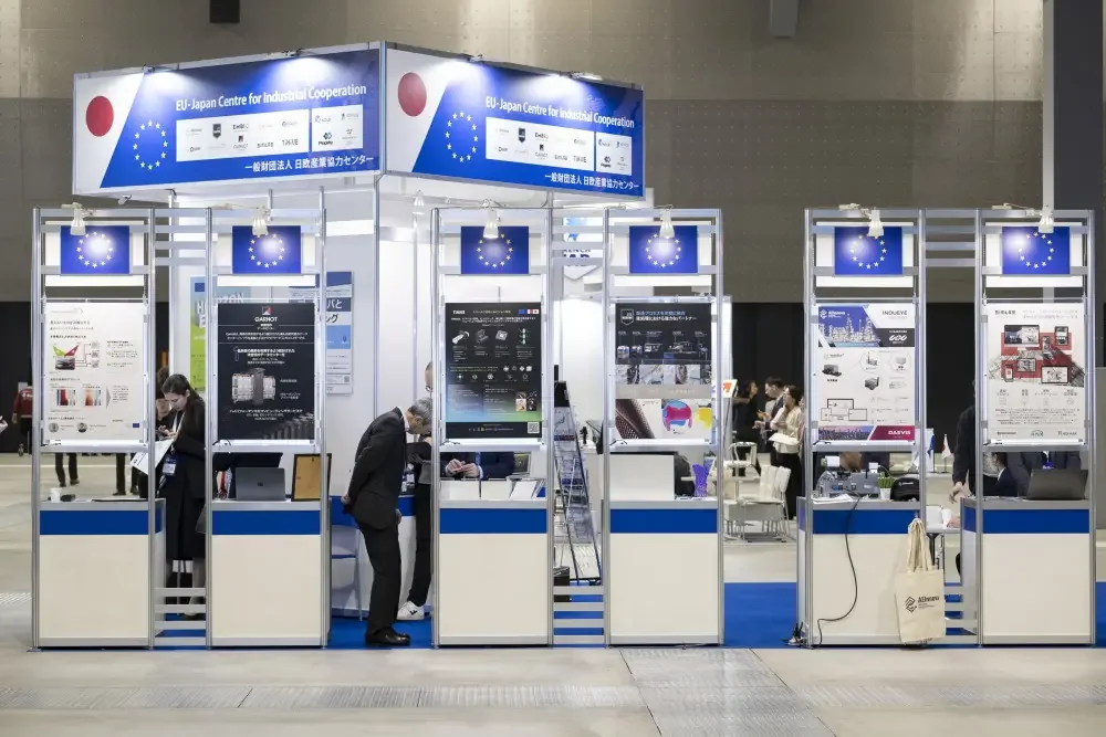 EU-Japan Centre for Industrial Cooperation booth with a row of exhibitor kiosks and posters, a SIMLAB poster on the far right