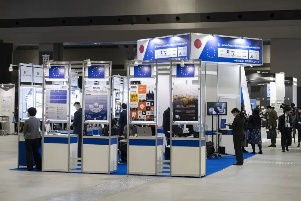 Wide view of the EU-Japan Centre for Industrial Cooperation booth with exhibitor kiosks and visitors in the exhibition hall