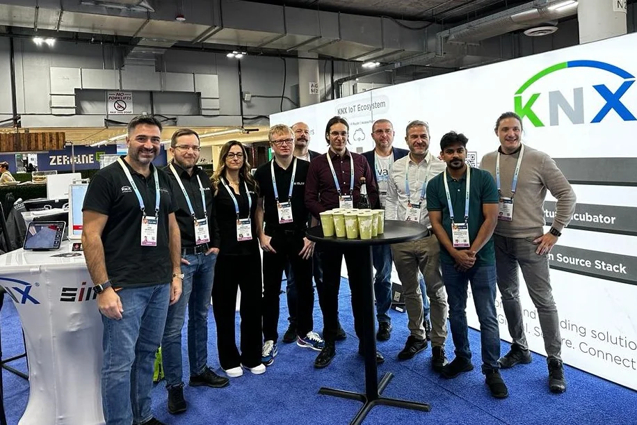Ten people with CES badges posing together at the KNX IoT Ecosystem booth at CES, beside a demo table covered with KNX and SIMLAB logos