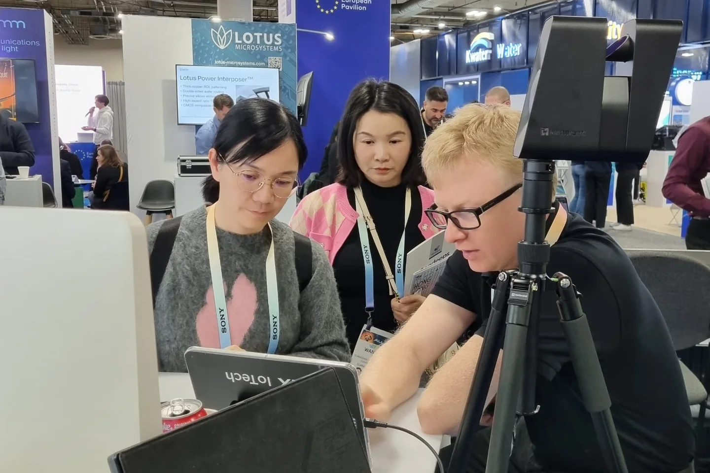 Exhibitor showing a tablet demo to two visitors at the CES booth, next to a Matterport camera mounted on a tripod