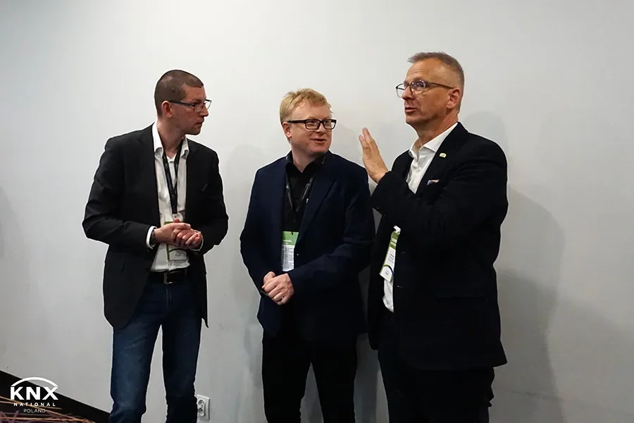 Three attendees with conference badges talking in front of a white wall at KNX Experts Meeting 2023