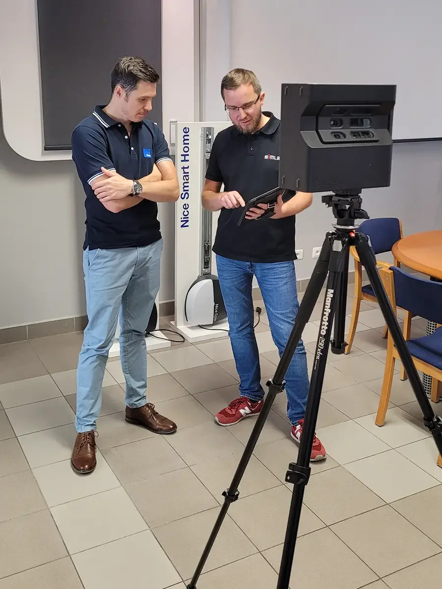 Nice representative and SIMLAB team member looking at a tablet next to a Matterport camera on a tripod, with a Nice Smart Home display stand behind them