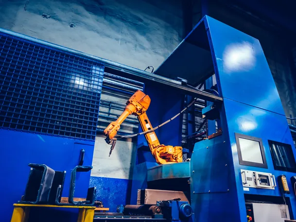 Orange industrial robot arm inside a blue production cell on a factory floor
