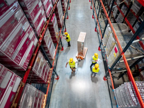 Overhead view of a warehouse aisle with high-bay pallet racking and workers in high-visibility vests moving a pallet