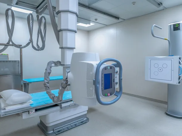 Empty hospital X-ray room with a ceiling-mounted radiography unit, patient table and wall detector stand