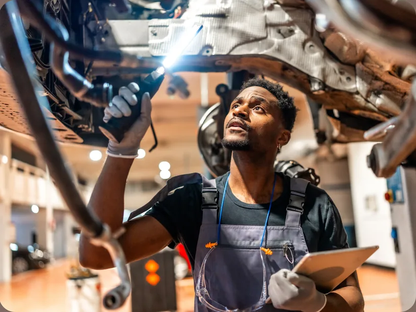 Technician with a flashlight and tablet inspecting the underside of a vehicle on a lift