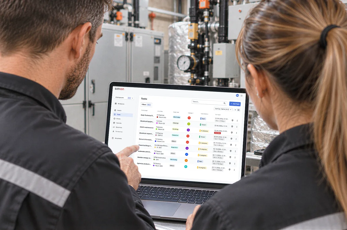 Two facility technicians in a plant room review a SIM-ON task list on a laptop